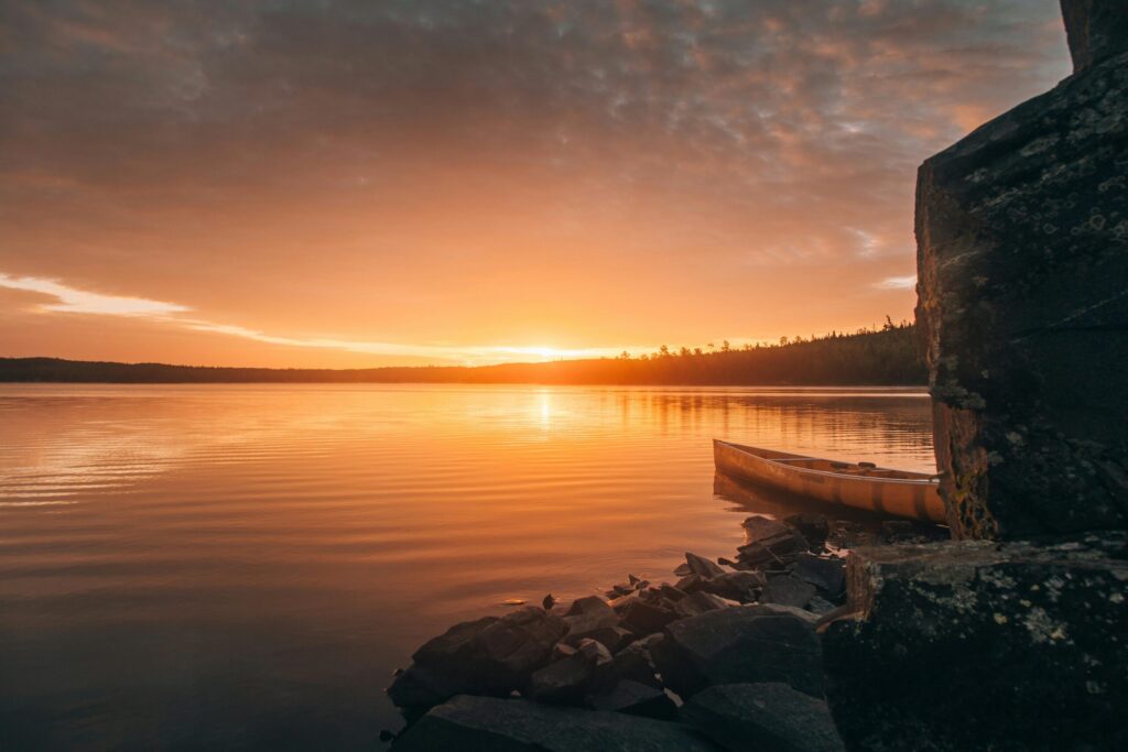 pexels-photo-2422479-2422479 A tranquil sunset over a lake in Ely, Minnesota, featuring a canoe by the rocky shore.