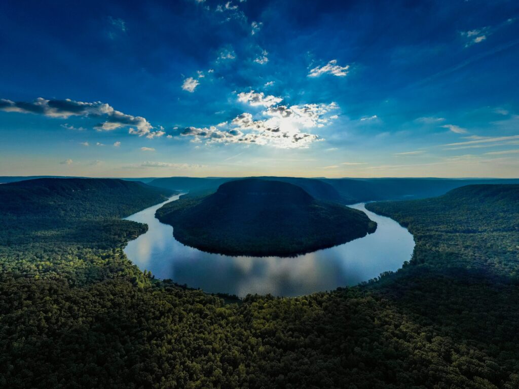 Stunning aerial view of a river curving through a lush forested valley under a vibrant sky.