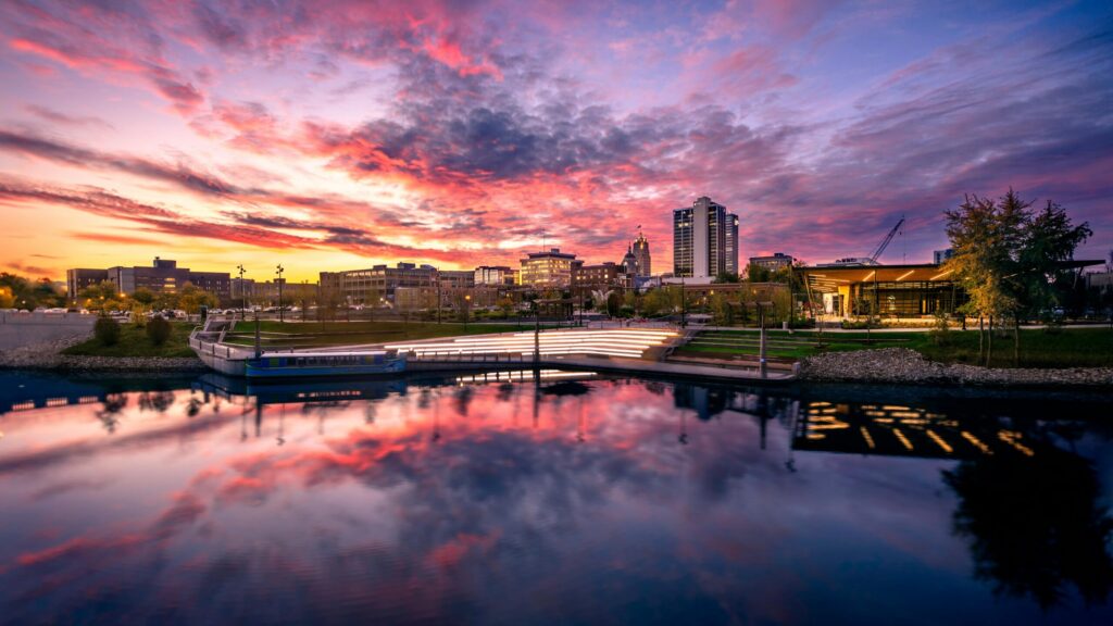 Beautiful sunset over Fort Wayne's skyline with reflections on the river, showcasing urban architecture.